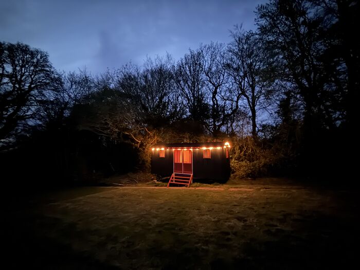 The lit shepherd's hut on the lawn at nightfall